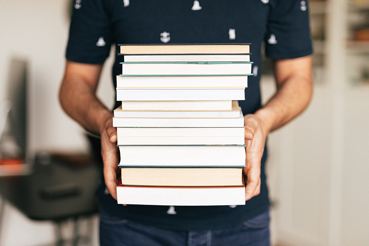 Close up of person holding a stack of library books.