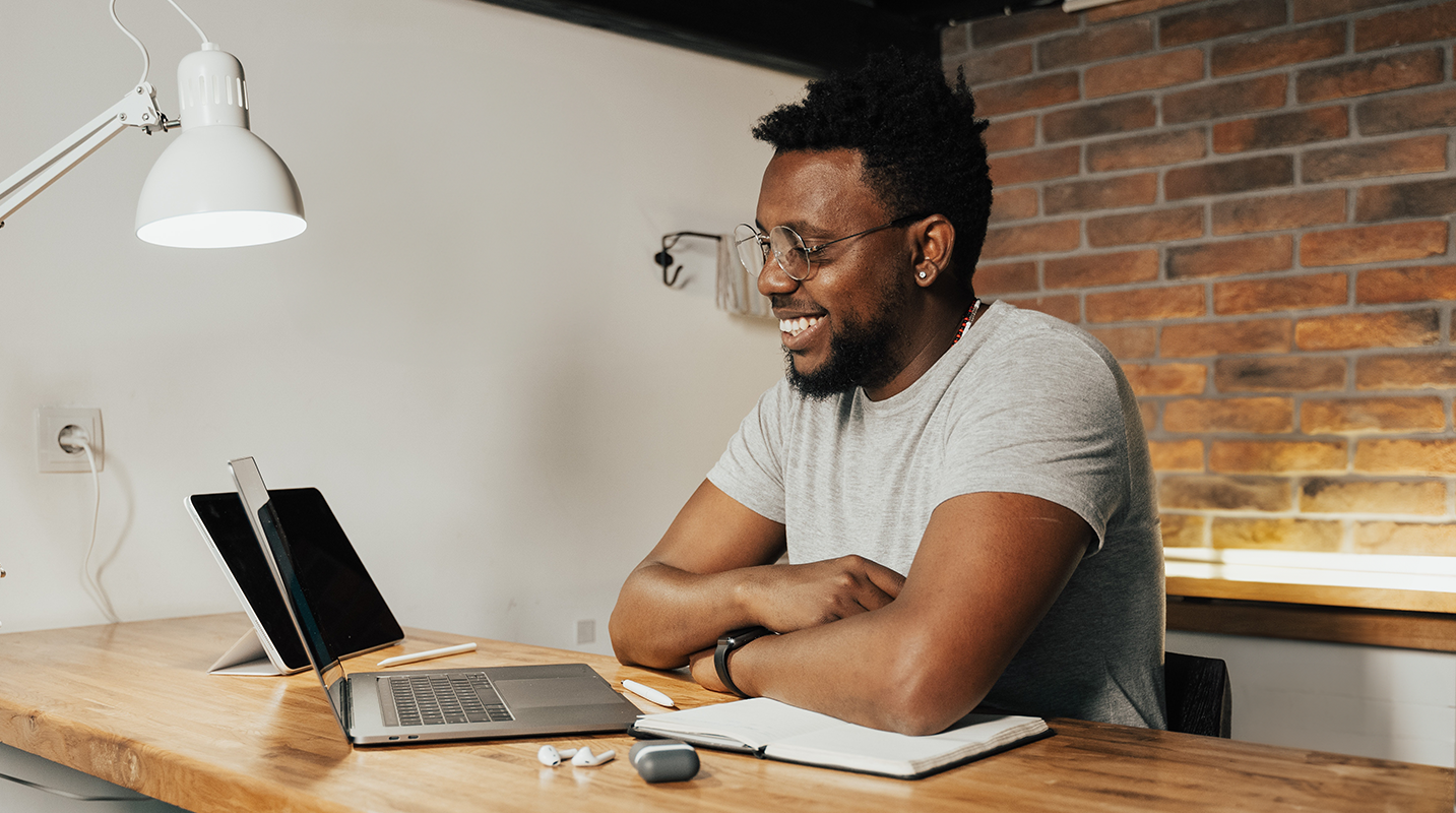 A man sitting at a desk, smiling at his laptop.